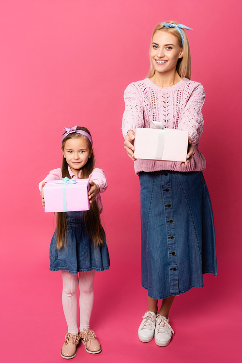 happy mother and daughter holding presents on pink