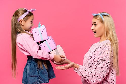 side view of amazed mother looking at daughter with presents isolated on pink