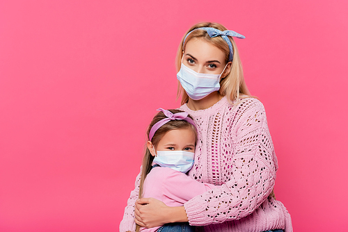 mother and daughter in medical masks  while hugging isolated on pink