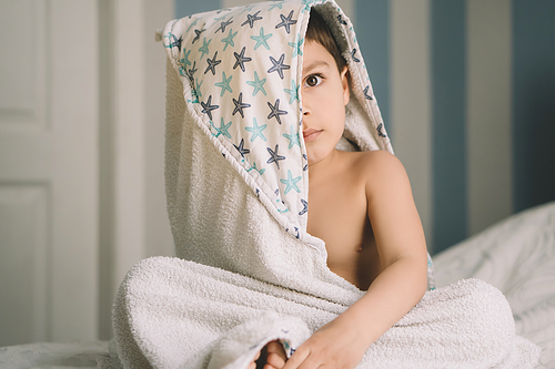 adorable boy, covered with hooded towel, sitting on bed and 