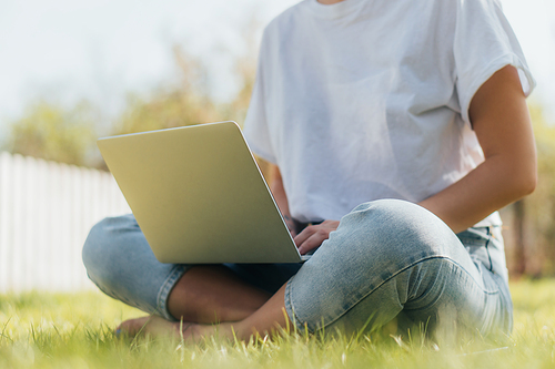 cropped view of freelancer sitting on green grass with laptop