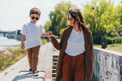 stylish mother and son in sunglasses holding hands while walking outside
