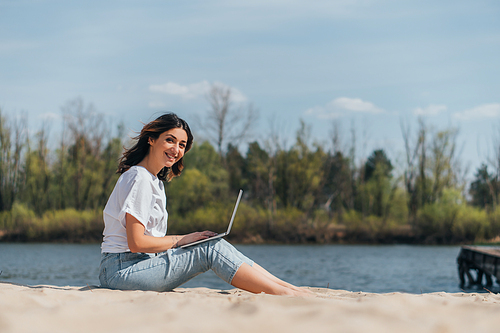 selective focus of happy freelancer using laptop near lake