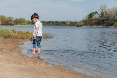 cute boy standing in lake near wet sand