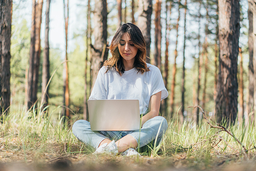 selective focus of freelancer using laptop while sitting in woods