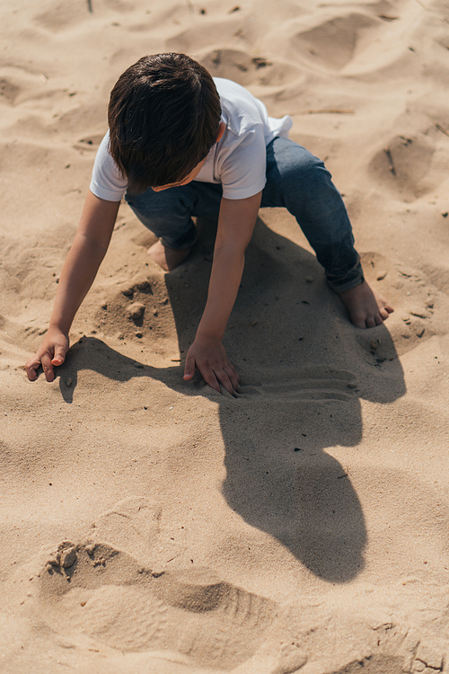 high angle view of boy sitting and touching sand