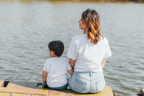 attractive mother sitting near cute son and lake
