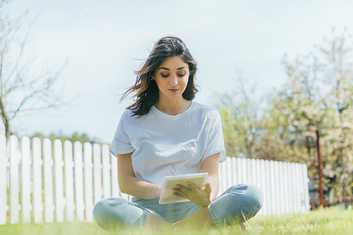 selective focus of woman using digital tablet and sitting on grass