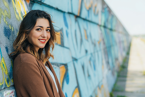 selective focus of cheerful woman smiling and  while standing near wall with graffiti