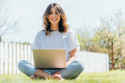 selective focus of happy freelancer sitting with laptop on grass