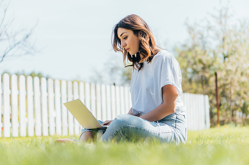 selective focus of beautiful freelancer using laptop and sitting on grass