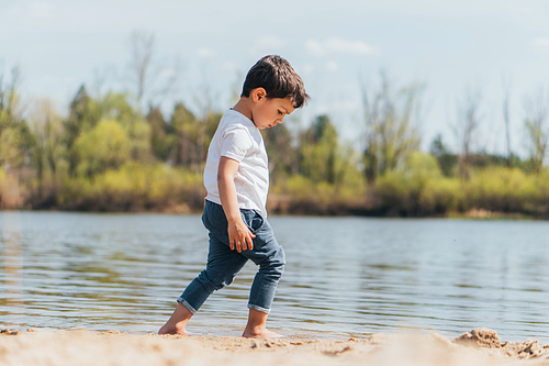 side view of barefoot boy walking on wet sand near pond