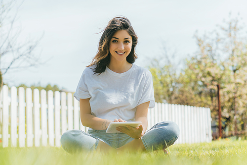 selective focus of happy woman using digital tablet and sitting on grass