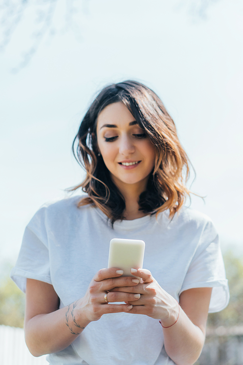 cheerful woman using smartphone and smiling outside