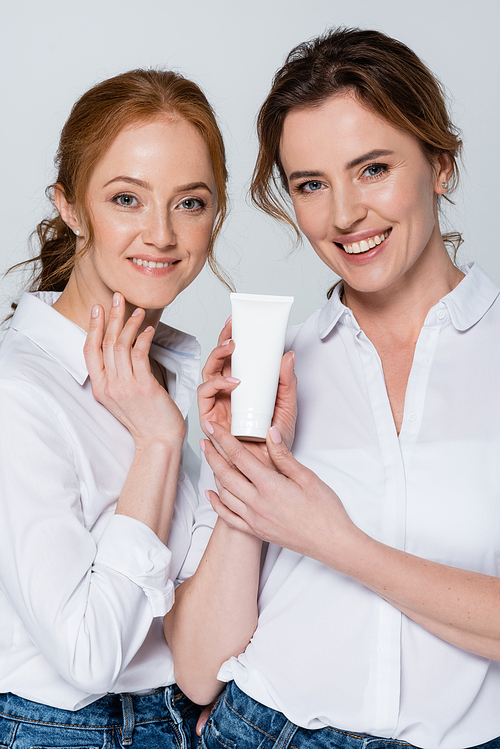 Cheerful women holding tube with cream isolated on grey