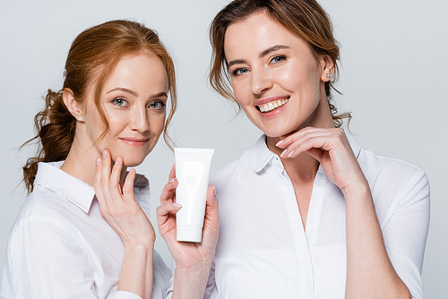 Smiling women  while holding tube with cream isolated on grey