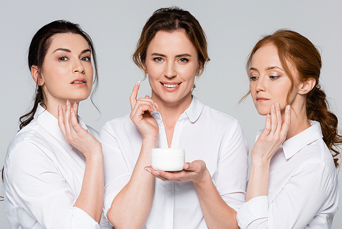 Smiling women applying cosmetic cream isolated on grey