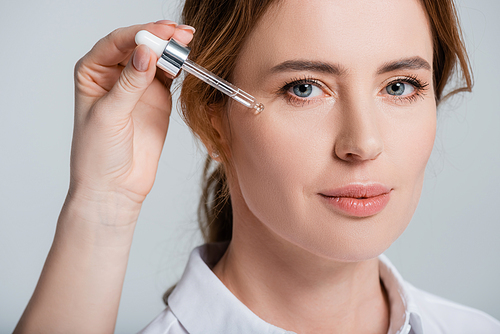 Female hand holding cosmetic serum near face of woman isolated on grey