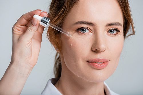 Female hand applying cosmetic serum of face of smiling woman isolated on grey