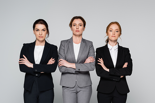 Adult businesswomen with crossed arms standing isolated on grey