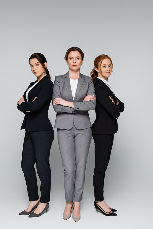 Businesswomen in suits standing with crossed arms on grey background