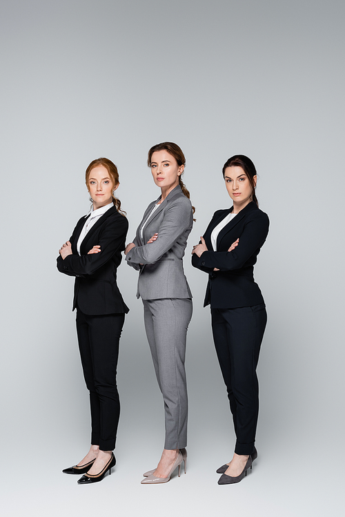 Adult businesswomen in suits  while standing on grey background