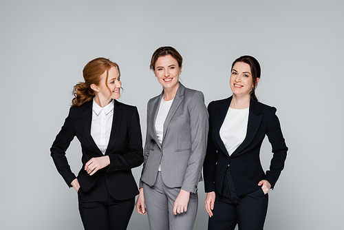 Smiling businesswomen with hands in pockets isolated on grey