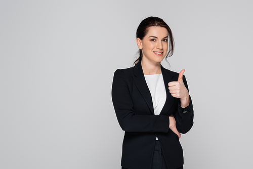 Smiling businesswoman in suit showing like gesture isolated on grey