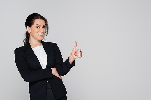 Businesswoman showing thumb up and smiling at camera isolated on grey