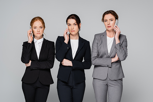 Confident businesswomen talking on smartphones isolated on grey