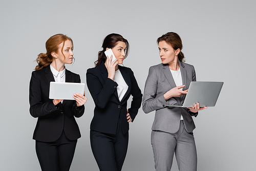 Businesswomen in formal wear using gadgets isolated on grey