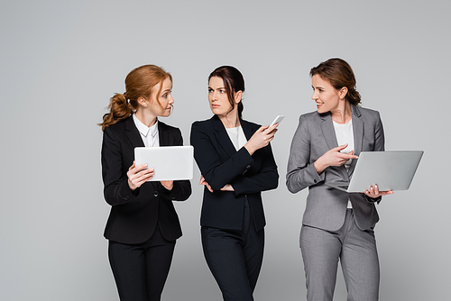 Businesswomen with devices looking at colleague with digital tablet isolated on grey