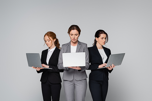 Confident businesswomen using laptops isolated on grey