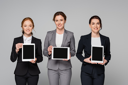 Smiling managers holding digital tablets isolated on grey