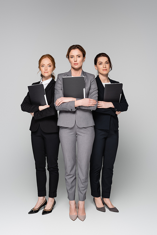 Confident businesswomen with paper folders standing on grey background