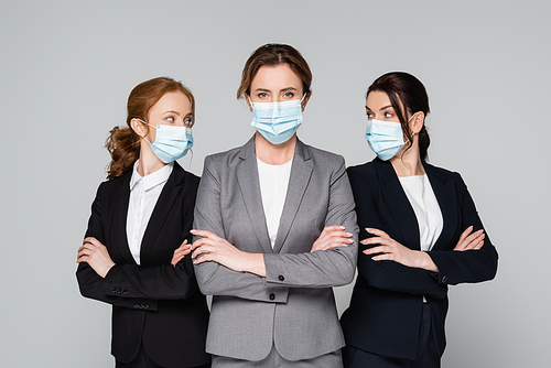 Businesswomen in medical masks standing with crossed arms isolated on grey