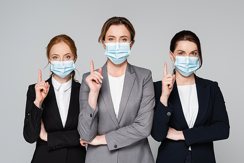 Businesswomen in medical masks pointing with fingers isolated on grey