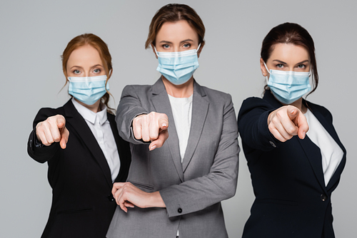 Businesswomen on blurred background in medical masks pointing with fingers isolated on grey