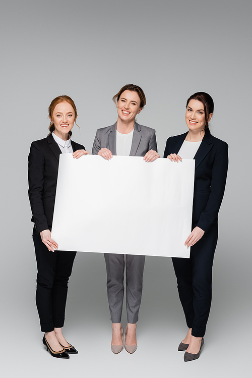 Cheerful businesswomen with white placard on grey background