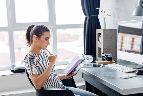 Young freelancer holding pen and notebook while working at home