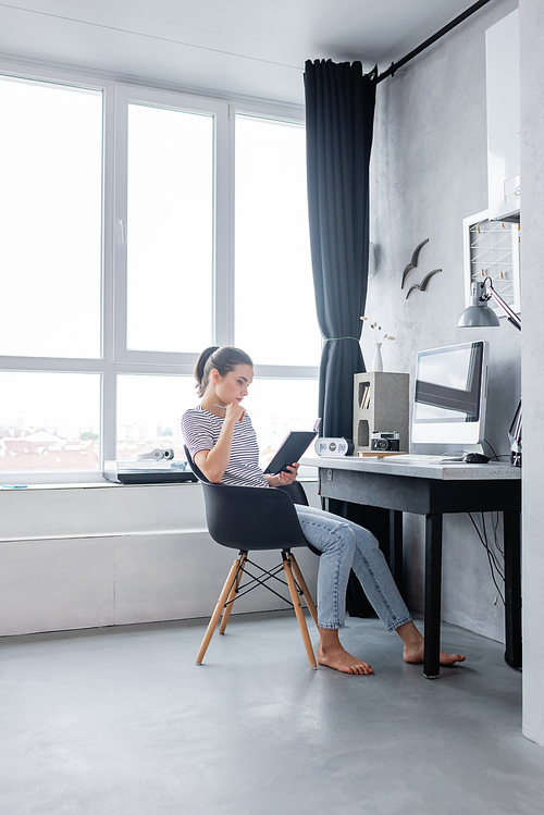 Brunette freelancer holding notebook near computer on table at home