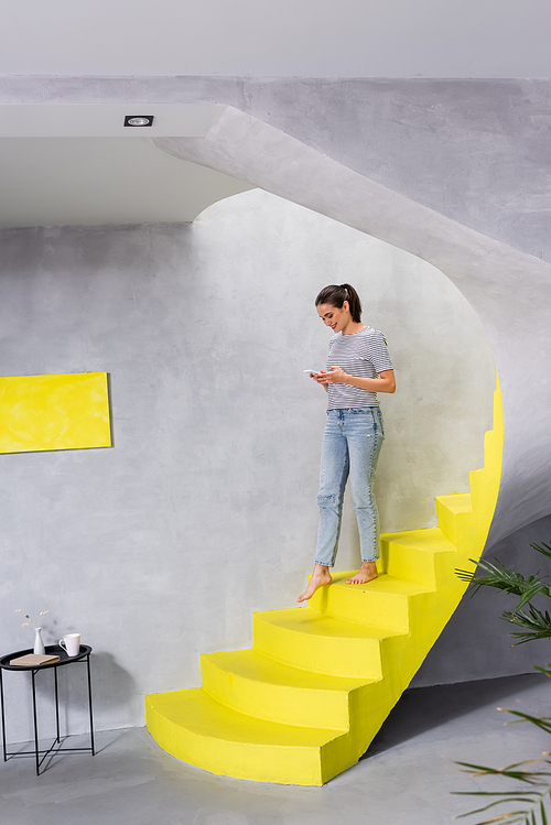 Selective focus of barefoot woman with smartphone walking on stairs at home