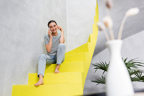 Selective focus of young woman talking on smartphone while sitting on stairs at home