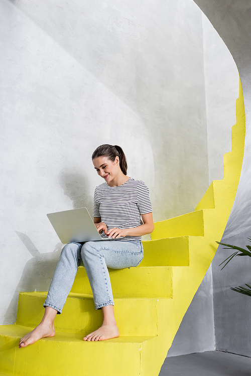 Barefoot freelancer using laptop on stairs at home