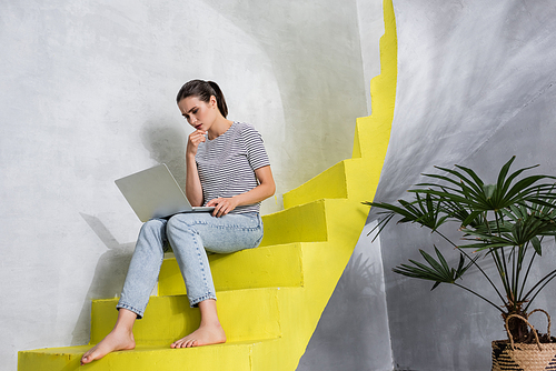 Pensive woman working on laptop while sitting on stairs at home