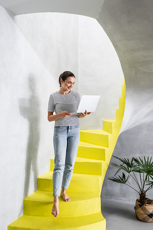 Young woman using laptop while walking on stairs at home
