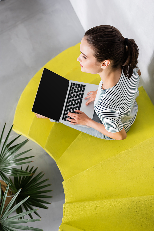 Overhead view of brunette freelancer using laptop while sitting on stairs at home