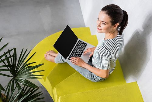 Overhead view of brunette woman with laptop sitting on stairs near plant