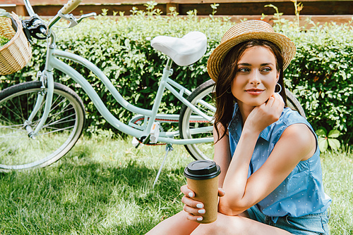 girl in straw hat holding paper cup and sitting near bicycle