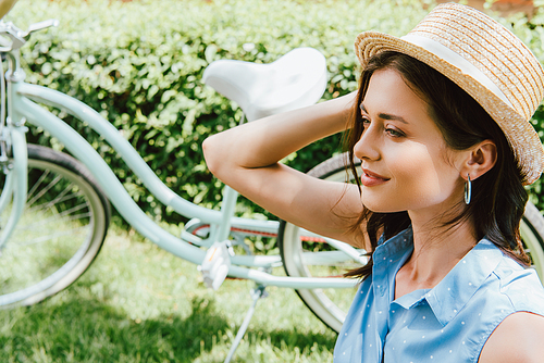 attractive woman touching straw hat near bicycle